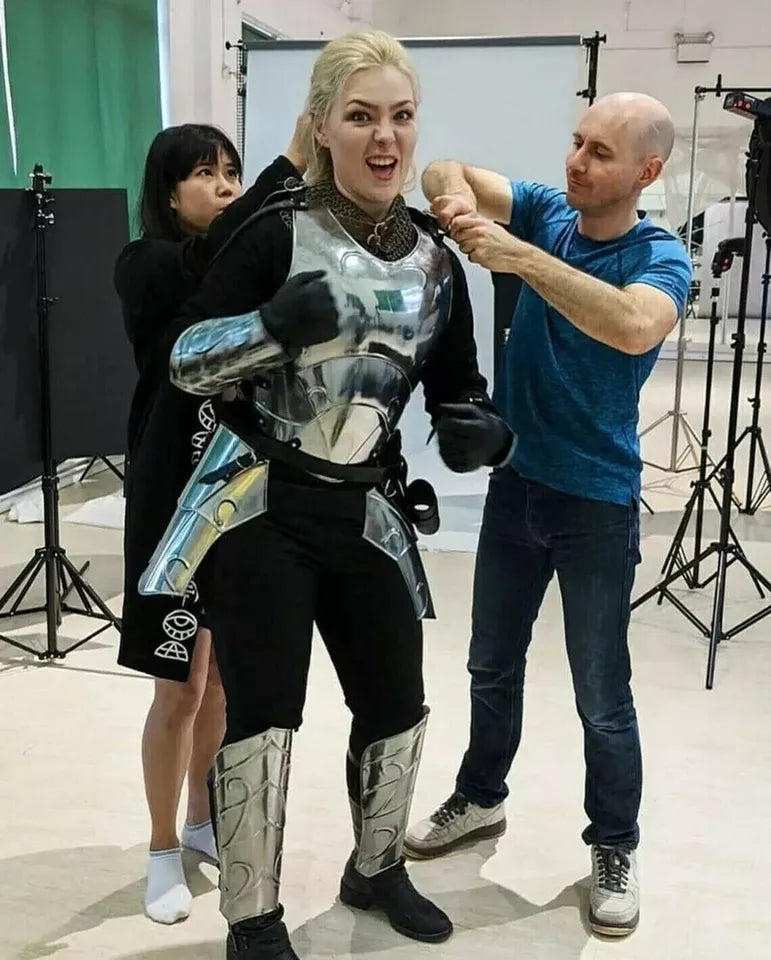 Behind-the-scenes shot of a blonde actress in sci-fi armor, assisted by crew, in a vibrant studio setup.